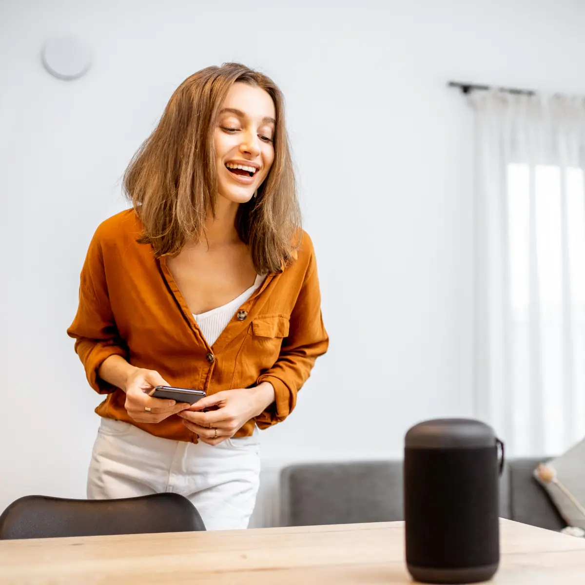 Happy woman using smart home speaker in modern living room with AI automation and voice control